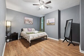 Ein Schlafzimmer mit einem Bett, einem Deckenventilator, einem Stehspiegel und zwei gerahmten Bildern an der Wand.