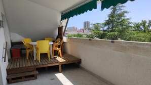 Ein Balkon mit Holzboden, gelben Stühlen, einem kleinen Tisch und einem grünen Markisenvorzelt.