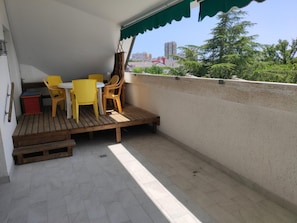 Ein Balkon mit Holzboden, gelben Stühlen, einem kleinen Tisch und einem grünen Markisenvorzelt.