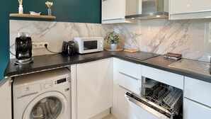 Cozinha compacta com máquina de lavar, micro-ondas e forno, parede de destaque em tom de azul-turquesa e bancada de madeira.