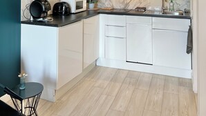 Uma cozinha moderna com armários brancos, painel de fundo de mármore e bancada preta.