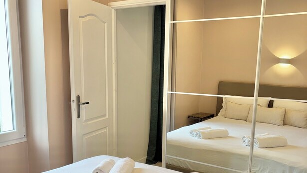 Quarto de hotel com uma cama grande, um espelho, uma porta e uma mesa de cabeceira.