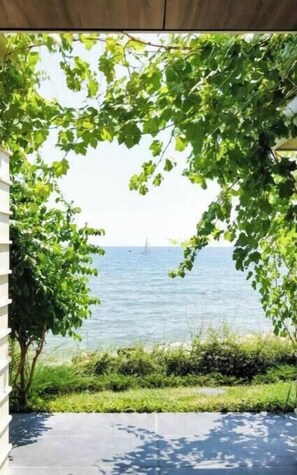 Blick durch eine Tür auf einen klaren Himmel und ein entferntes Segelboot auf dem Wasser.
