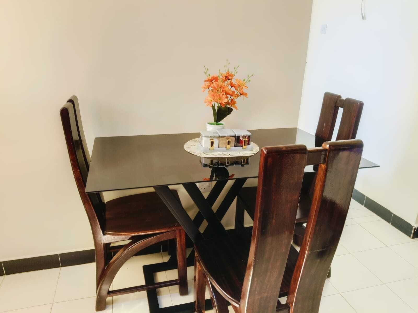 A dining table with four chairs, a vase with flowers, and a small decorative item on the table.