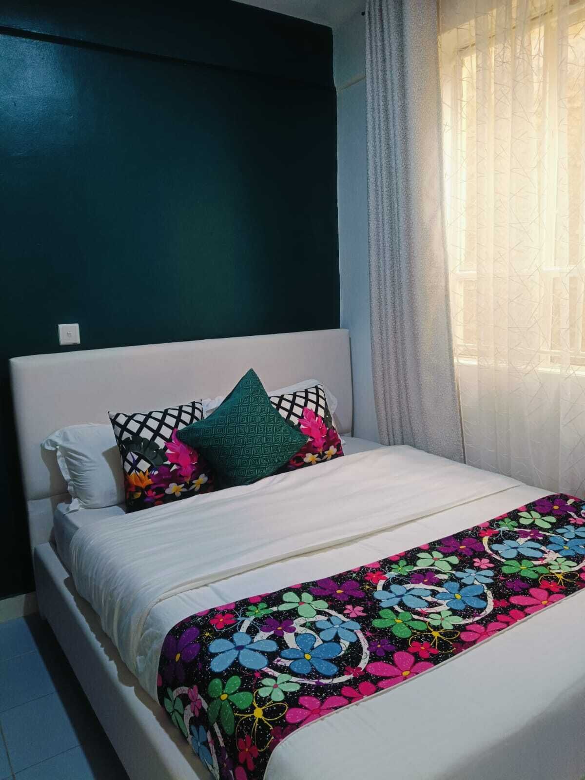 A bed with a floral bedspread, a white pillow, and a green pillow.
