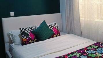 A bed with a floral bedspread, a white pillow, and a green pillow.