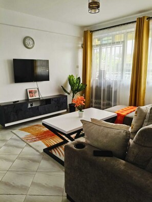A modern living room with a flat-screen TV, a sofa, a coffee table, and a plant. - Soulful short & long stays in Nakuru, Rooftop views,cozy rooms, peace & purpose. (Nakuru)