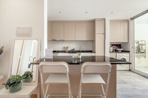 Una cocina moderna con una isla central, sillas blancas y vistas a través de un ventanal amplio.