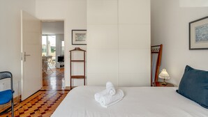 Ein Hotelzimmer mit Bett, Sessel, Tisch, Lampe und einem gerahmten Bild an der Wand.
