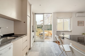 A modern kitchen with a dishwasher, a sink, and a dining area with chairs and a table. - Santar M Terrace by Homing (Santarém)