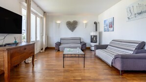 Una sala de estar con una mesa de centro de madera, dos sofás, un televisor y obras de arte en las paredes.
