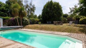 Piscina con muelle de madera, rodeada de follaje y árboles.