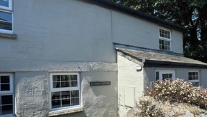 Een stenen vakantiehuisje met een bordje waarop 'St James Cottage' staat, een stenen muur en een houten hek.
