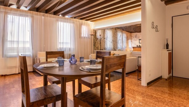 Un comedor con una mesa redonda de madera, sillas y una cocina al fondo.