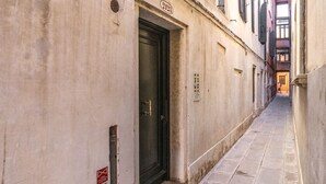 Un callejón estrecho con una puerta cerrada, un letrero encima de la puerta y una tubería en la pared.
