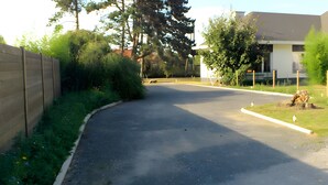En uppfart till ett bostadshus med ett trästaket, grönska och en modern byggnad i bakgrunden.