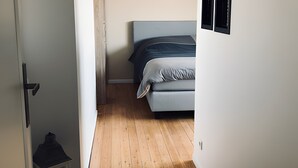 En smal hall leder till ett sovrum med en säng, en vit dörr och ett litet vitt skåp.