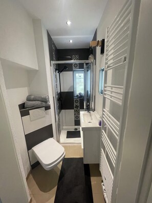 Ein kleines Badezimmer mit Toilette, Waschbecken, Dusche und Handtuchhalter.