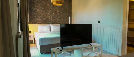 Un dormitorio con una cama, un televisor sobre un mueble bajo, una mesa blanca y una lámpara de techo tejida.