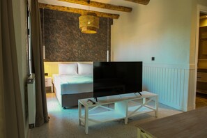 Un dormitorio con una cama, un televisor sobre un mueble bajo, una mesa blanca y una lámpara de techo tejida.