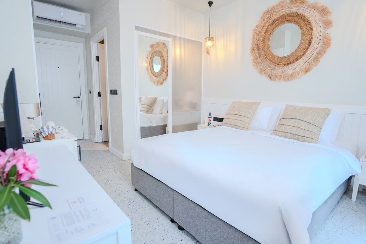 A modern bedroom with a large bed, a bedside table, a mirror, and a wall-mounted light fixture.
