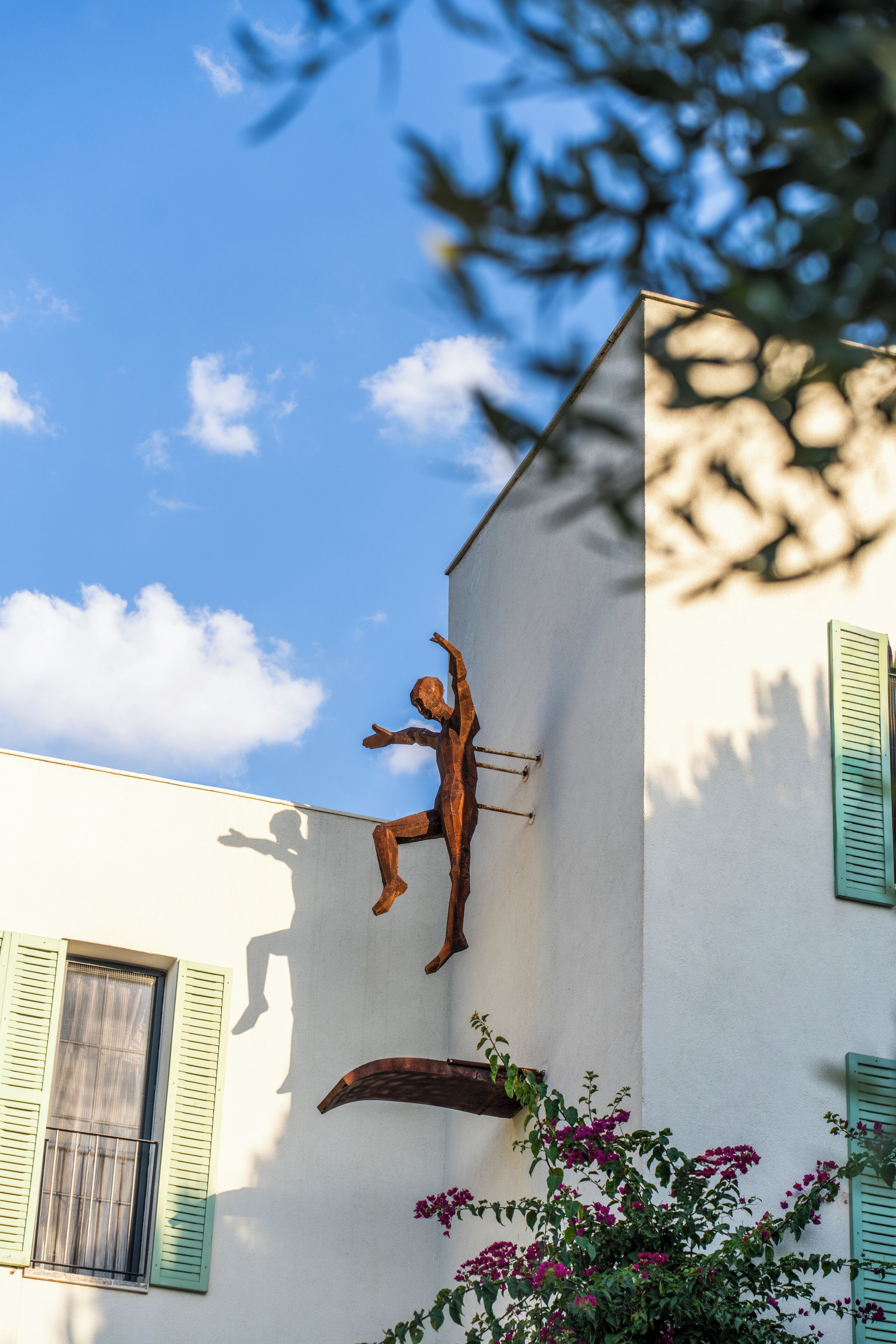 A building with a sculpture of a figure in a dynamic pose, attached to the exterior wall.