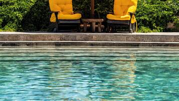 A pool with two yellow chairs and a table under a yellow umbrella.