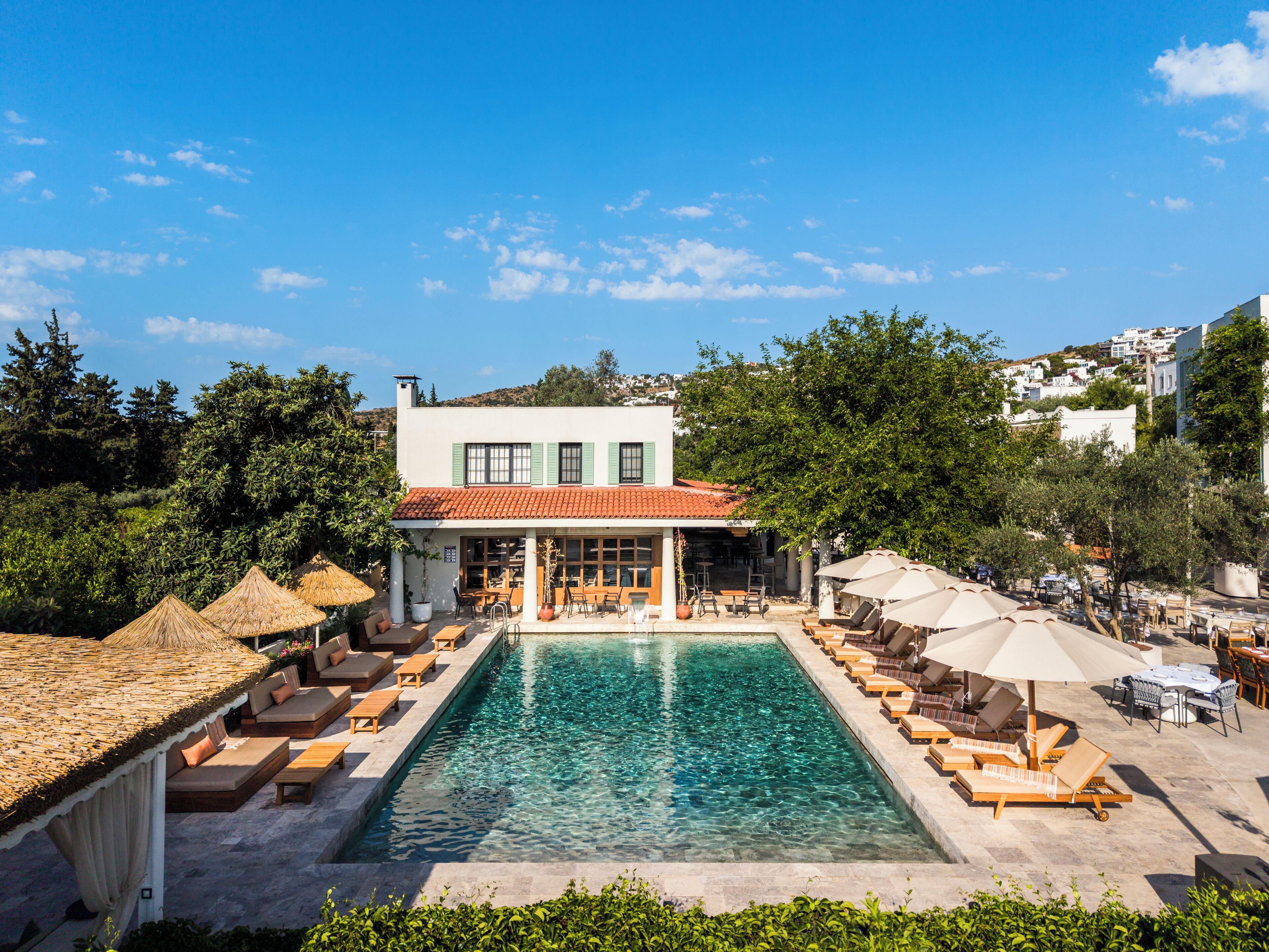 A poolside area with lounge chairs and umbrellas, a building with a red-tiled roof, and a clear blue sky.