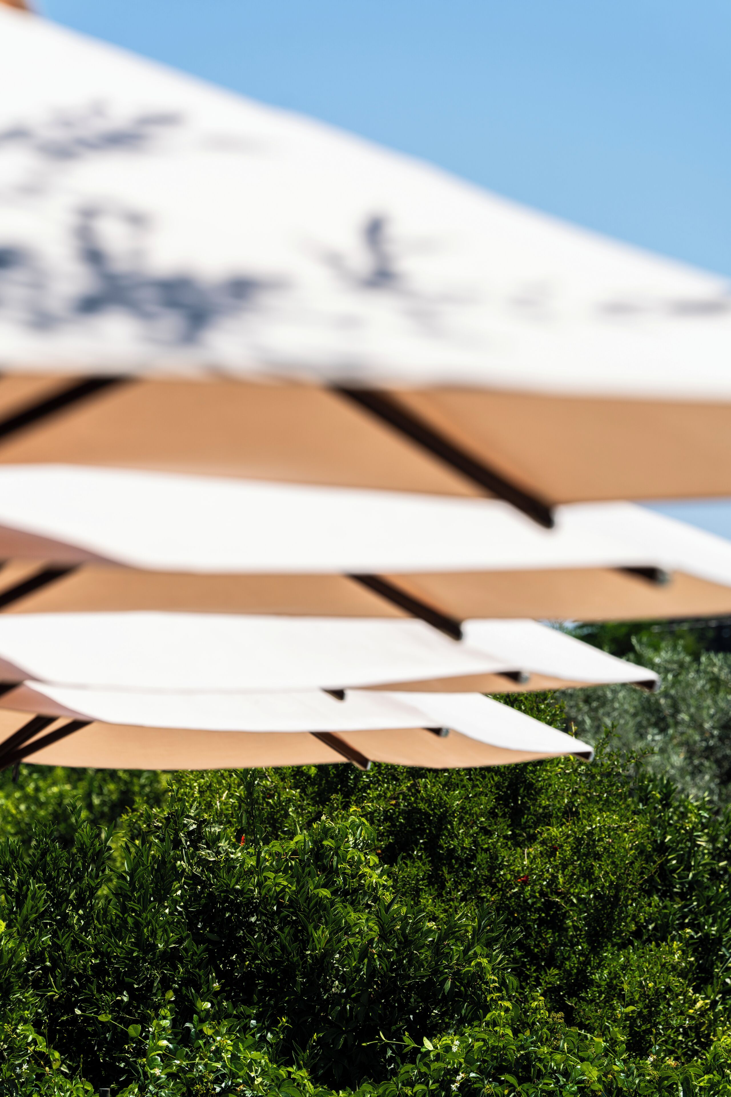 A close-up of a beach umbrella structure with a blurred background of green foliage.