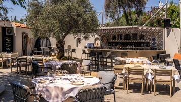 An outdoor dining area with tables and chairs, a bar, and a view of trees and buildings.