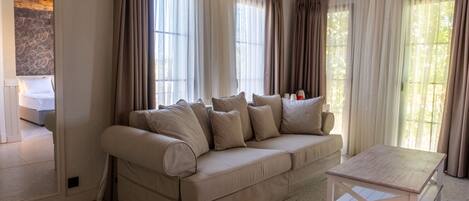 A spacious living area with a beige sofa, a wooden coffee table, and large windows with sheer curtains.