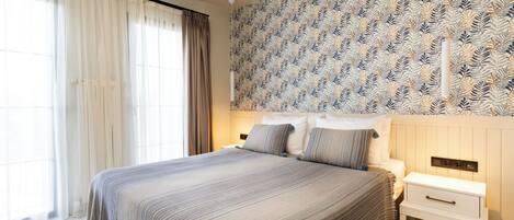 A bedroom with a large bed, a nightstand, a wall-mounted light fixture, and a patterned wallpaper.