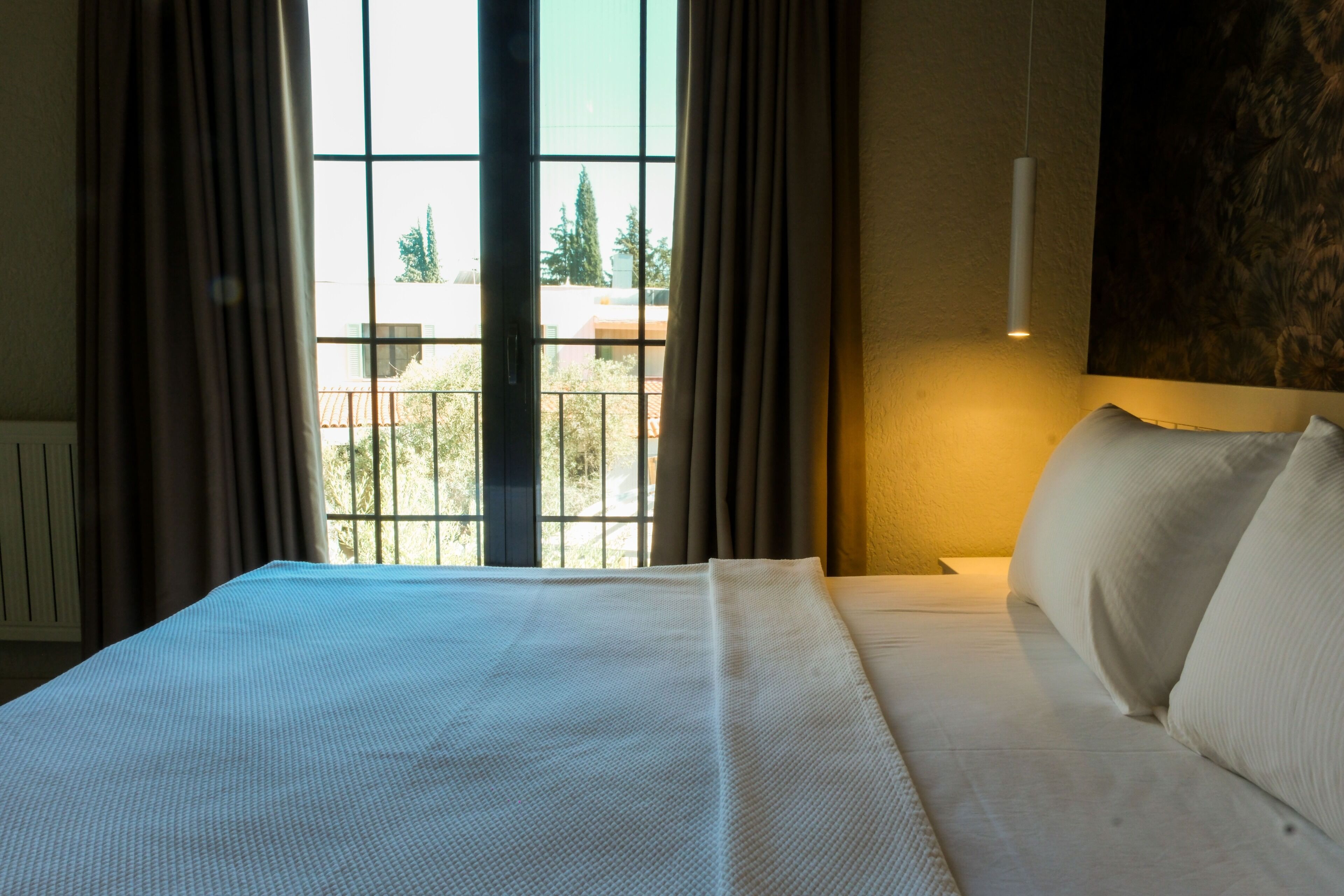 Una habitación de hotel con una cama grande, vista por la ventana y una lámpara fijada a la pared.