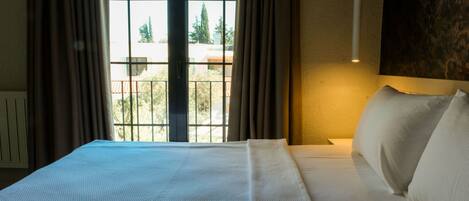 Una habitación de hotel con una cama grande, vista por la ventana y una lámpara fijada a la pared.