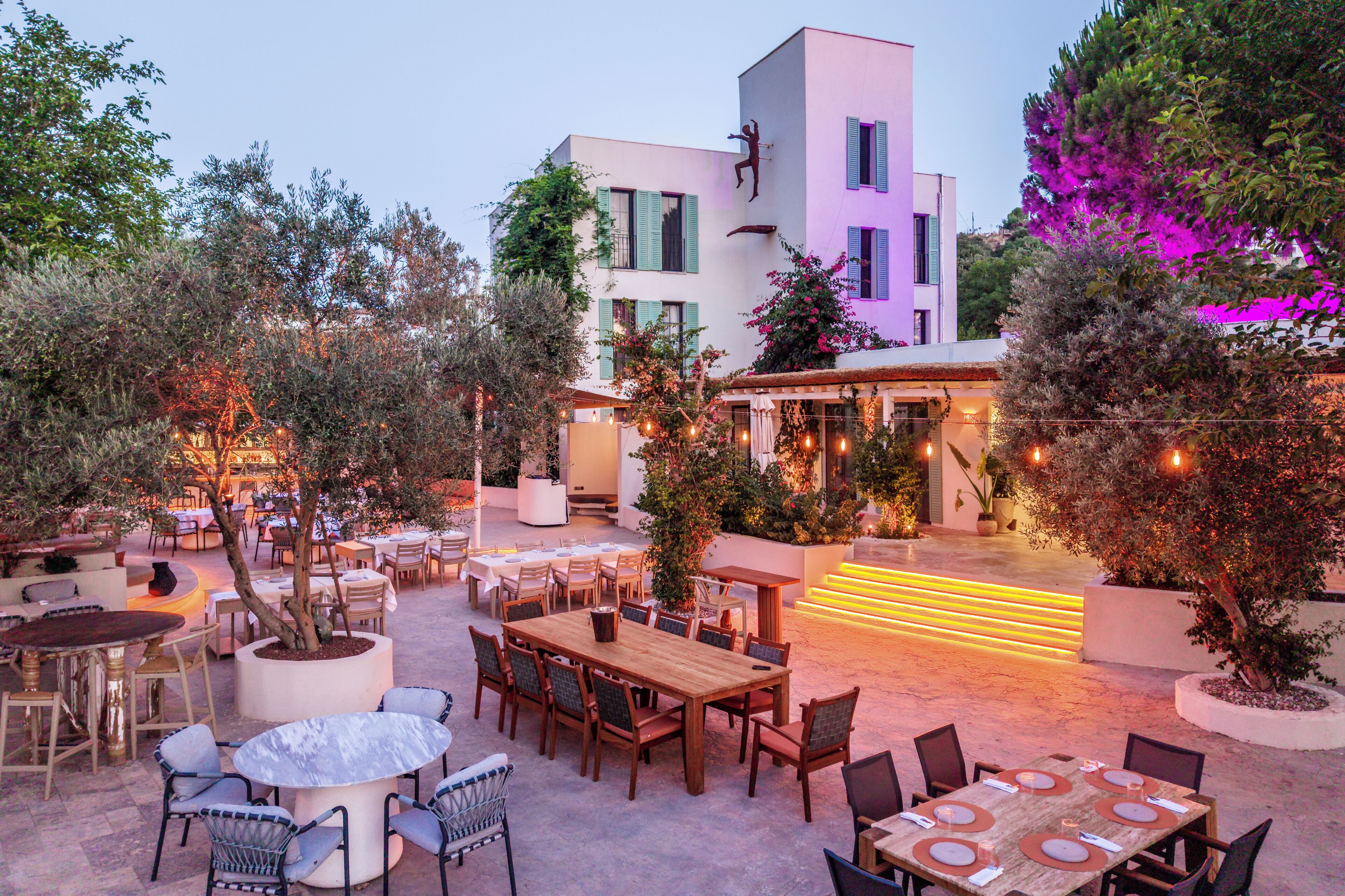An outdoor dining area with multiple tables and chairs, surrounded by potted plants and trees.