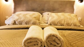 A neatly made bed with a headboard, two wall-mounted light fixtures, and a rolled towel on the bed. - BP Gołd Premium (Toruń)