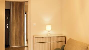 A room with a wooden floor, a sofa, a lamp, and a ceiling light fixture.