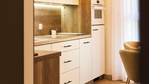 A modern kitchen with wooden cabinetry, a built-in oven, and a dining area with a chair. - BP Gołd Premium (Toruń)