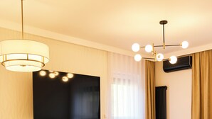 A modern hotel room with a flat-screen TV, a dining area with a table and chairs, a sofa, and a chandelier. - BP Gołd Premium (Toruń)