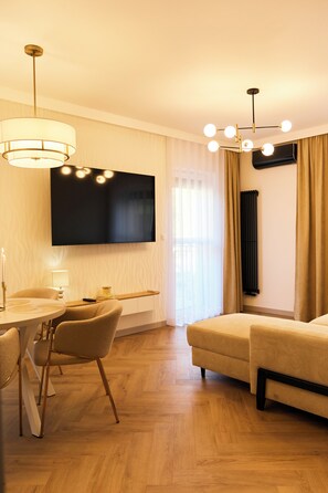 A modern hotel room with a flat-screen TV, a dining area with a table and chairs, a sofa, and a chandelier. - BP Gołd Premium (Toruń)