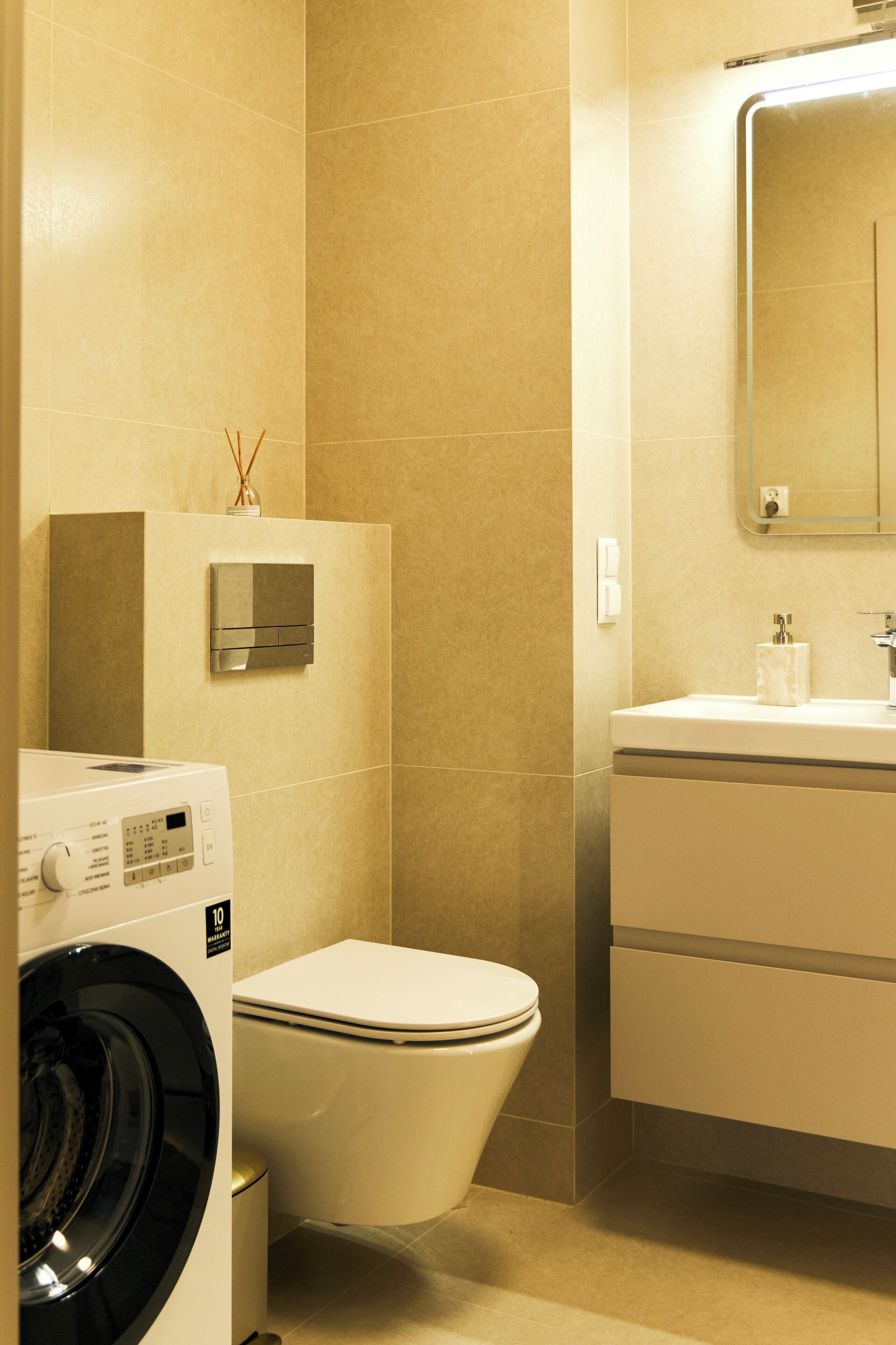 Un baño con lavadora, inodoro y lavamanos con espejo superior.