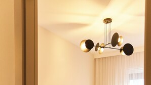 A modern living room with a sofa, a ceiling light fixture, and a window with curtains. - BP Gołd Premium (Toruń)