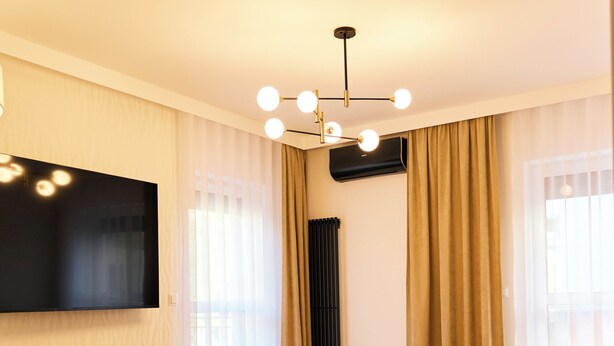 A modern living room with a sofa, a TV mounted on the wall, a wooden floor, and a ceiling light fixture. - BP Gołd Premium (Toruń)
