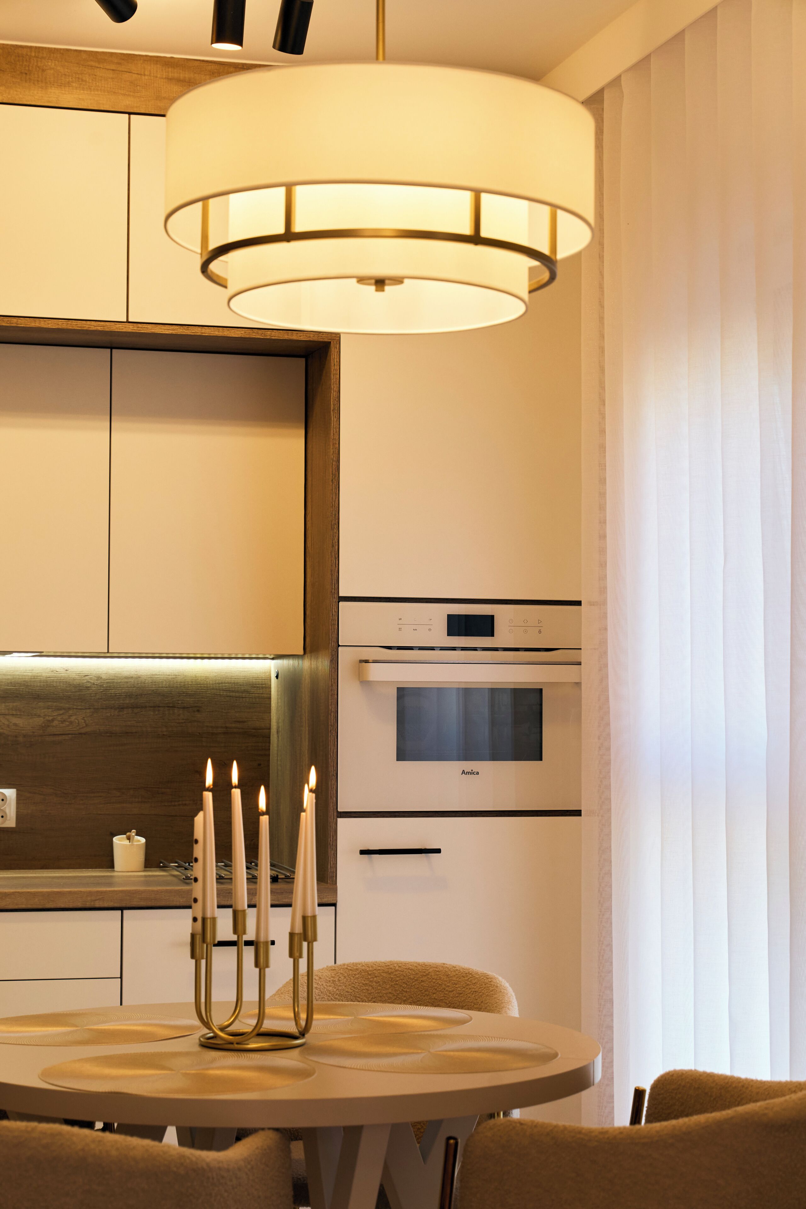 A modern kitchen with a round dining table, a chandelier, and a built-in oven.