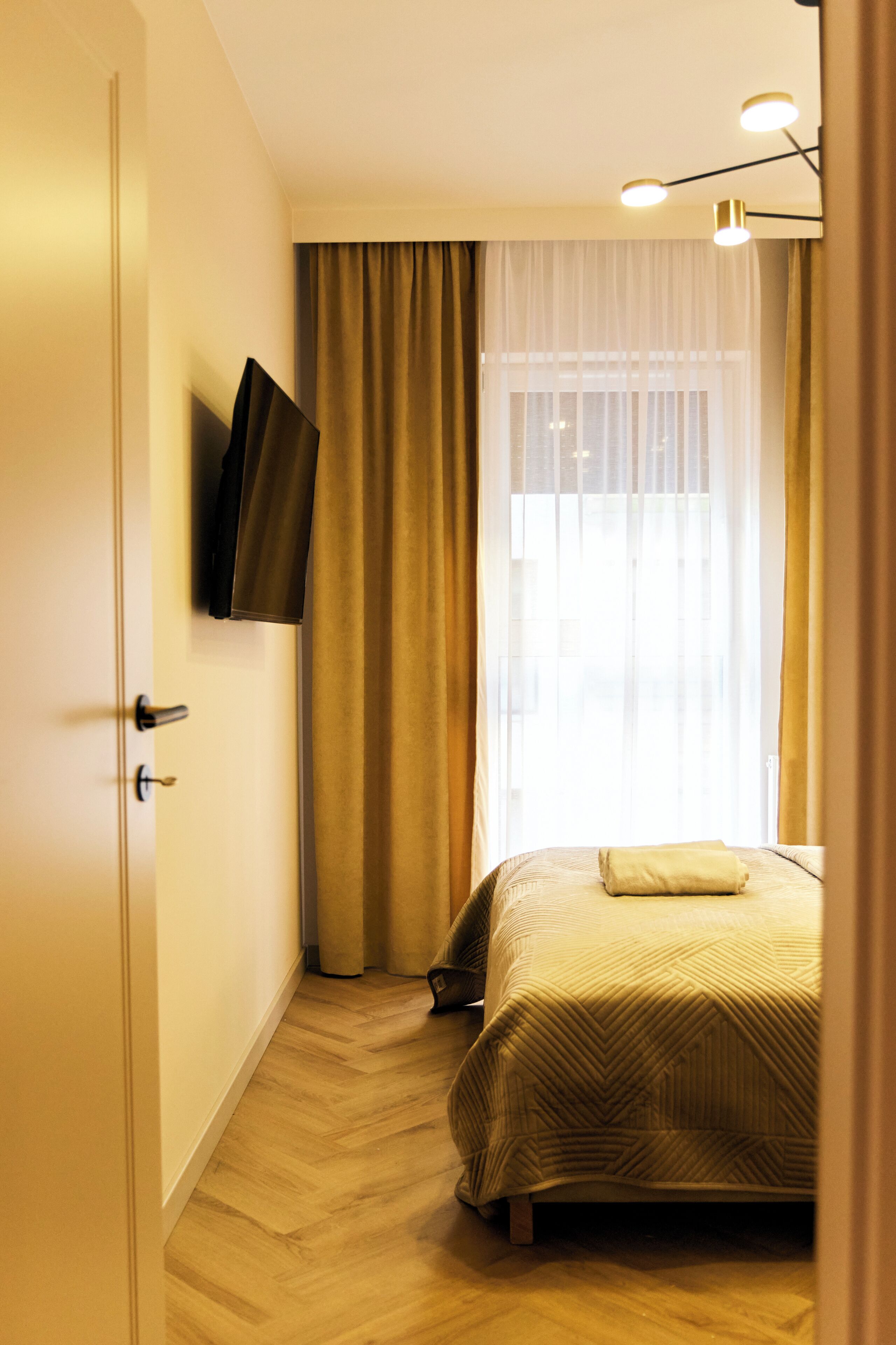 A hotel room with a bed, a television mounted on the wall, and a window with curtains.