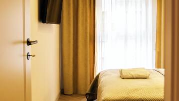 A hotel room with a bed, a television mounted on the wall, and a window with curtains.