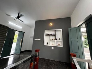 Ein modernes Interieur mit dunklem Marmorboden, Deckenventilator, einer Wandablage mit Dekoration und einer Tür, die nach draußen führt.