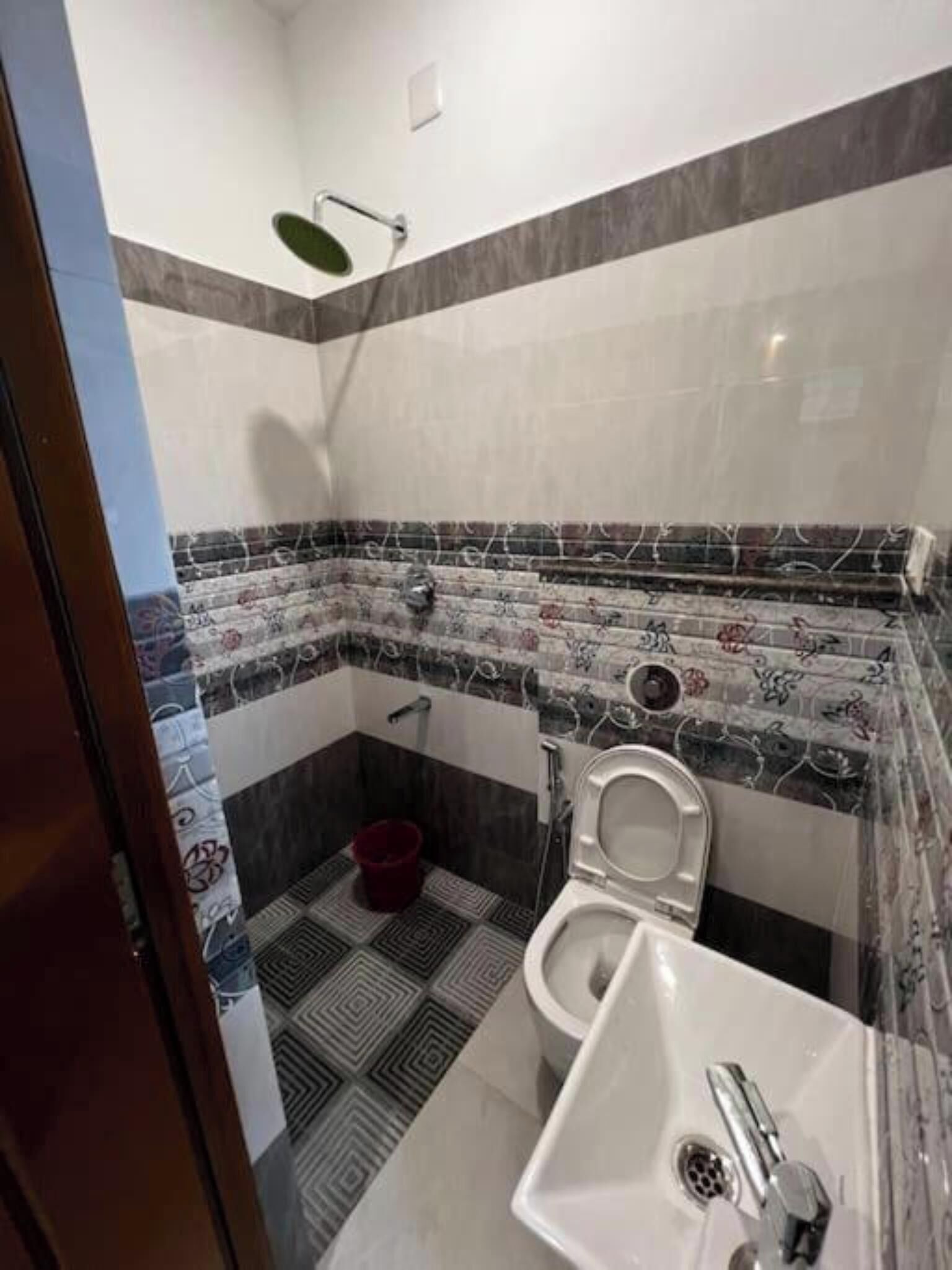A bathroom with a toilet, sink, shower, and patterned tiles.