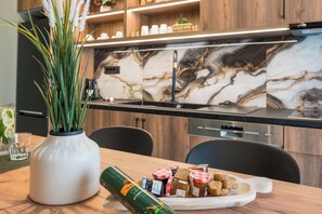 Eine moderne Küche mit Marmor-Spritzschutz, einer weißen Vase mit Grünpflanzen und verschiedenen Lebensmitteln auf einem Holztisch.
