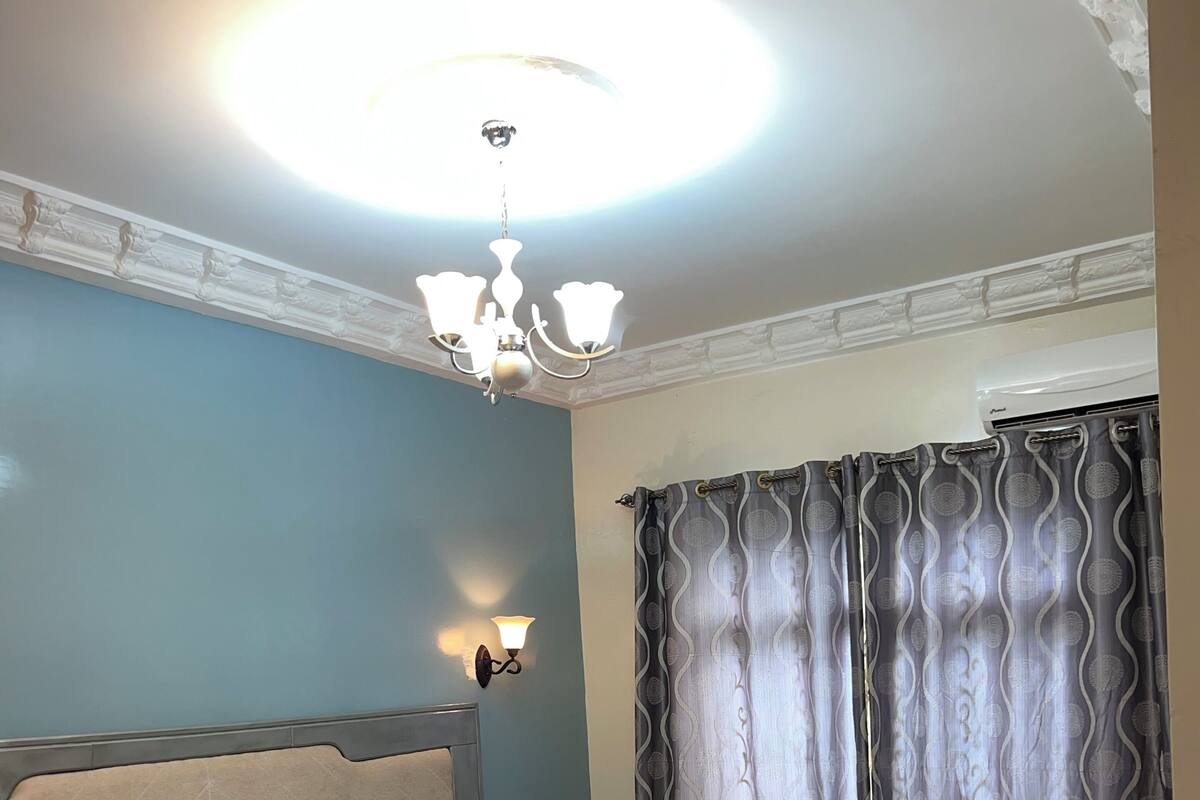 A bedroom with a bed, a desk, a chair, a rug, and a ceiling light.